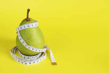 Measuring tape and green ripe pear on yellow background with space for text. Healthy eating and...