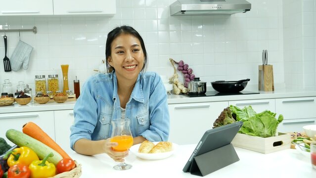 Happy asian woman eating healthy food drinks watch online movie. Women enjoy video call web conference live streaming home kitchen use digital tablet. Female use smart phone online call social media
