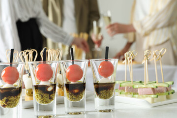 Many different tasty canapes on white table. People enjoying buffet meals indoors, closeup