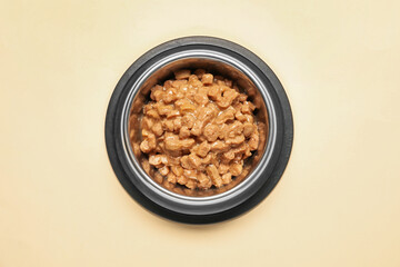 Wet pet food in feeding bowl on pale yellow background, top view