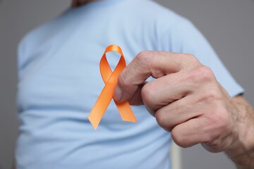 Multiple Sclerosis awareness. Senior man with orange ribbon on grey background, closeup