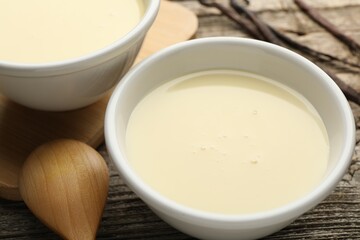 Tasty condensed milk, spoon and vanilla pods on wooden table, closeup