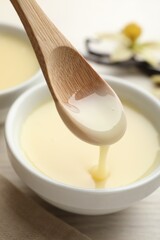 Taking tasty vanilla condensed milk with spoon from bowl on white wooden table, closeup