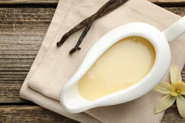 Tasty condensed milk, vanilla pods and flower on wooden table, flat lay