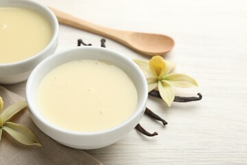 Tasty condensed milk, vanilla pods, flowers and spoon on white wooden table, closeup