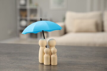 Human figures under umbrella on grey table indoors. Insurance concept