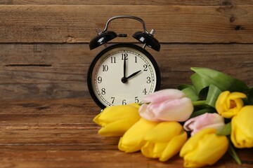 Spring time. Alarm clock and beautiful tulips on wooden table