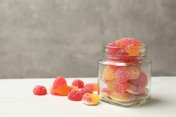 Tasty jelly candies in glass jar on white table against grey background. Space for text