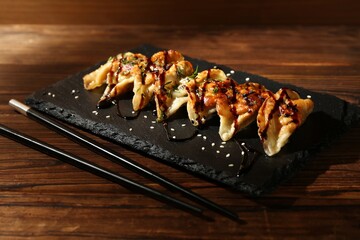 Tasty fried gyoza (dumplings) and chopsticks on wooden table, closeup
