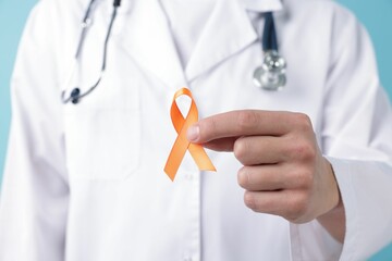 Multiple Sclerosis awareness. Doctor with orange ribbon on light blue background, closeup