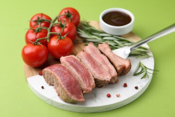 Delicious sliced beef tenderloin with different degrees of doneness, tomatoes, sauce and spices on green table, closeup