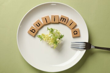 Plate with word Bulimia, lettuce and fork on olive background, top view
