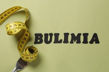 Word Bulimia, measuring tape and fork on olive background, top view