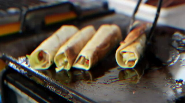 Tentu, ini deskripsi gambar dalam bahasa Inggris:
This image shows four shawarmas, also known as wraps, lined up on a dark griddle. The shawarmas are made with a light-colored flatbread that is rolled