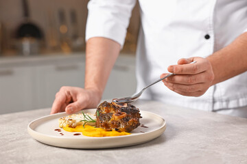 Professional chef adding sauce to delicious dish at table indoors, closeup