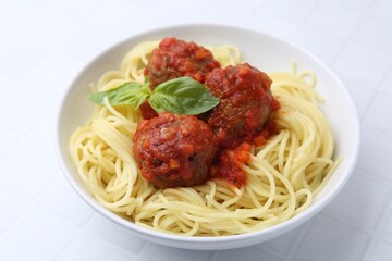 Delicious pasta with meatballs in bowl on white tiled table, closeup