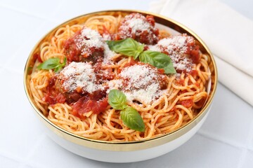 Delicious pasta with meatballs, cheese and basil in bowl on white tiled table, closeup
