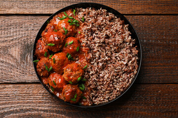 Tasty meatballs with sauce and brown rice on wooden table, top view