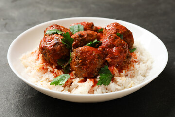 Tasty meatballs with sauce and rice on black table, closeup