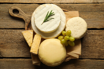 Different types of cheese, rosemary and grapes on wooden table, top view