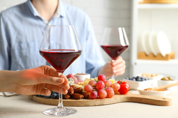 Women holding glasses of wine at light grey table with different snacks indoors, closeup