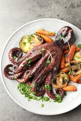 Roasted octopus with vegetables and mushrooms on grey table, top view