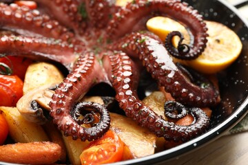 Fried octopus with lemon and vegetables in pan on wooden table, closeup