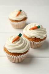 Tasty carrot muffins with cream on white wooden table, closeup