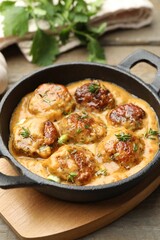 Delicious meatballs with gravy cream sauce and herbs on wooden table, closeup