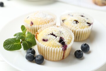 Delicious muffins with blueberries, powdered sugar and mint on white table, closeup