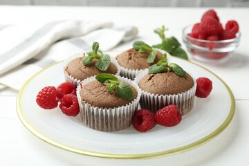 Delicious muffins with raspberries and mint on white table, closeup