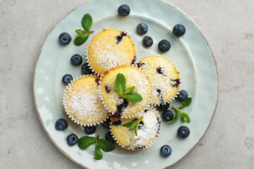 Delicious muffins with blueberries, powdered sugar and mint on grey textured table, top view