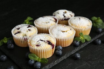 Delicious muffins with blueberries, powdered sugar and mint on dark textured table, closeup