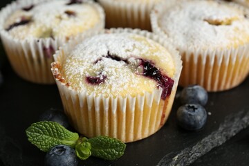 Delicious muffins with blueberries, powdered sugar and mint on dark table, closeup