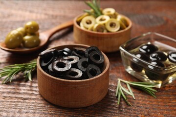 Different delicious marinated olive rings and rosemary on wooden table, closeup