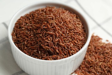 Raw brown rice in bowl on table, closeup
