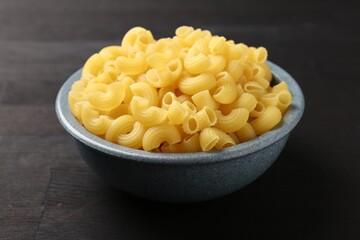 Raw horns pasta in bowl on dark wooden table, closeup