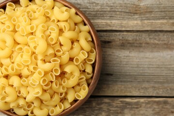 Raw horns pasta in bowl on wooden table, top view. Space for text