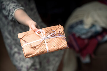 woman's hand presents a rectangular gift wrapped in yellow mesh craft paper, showcasing a thoughtful gesture perfect for special occasions