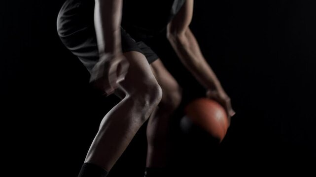 Basketball player bouncing a ball. African american sports man practicing against black background. Abstract body shot side view.