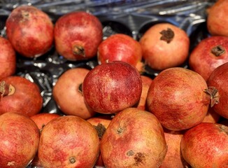 Lots of ripe red pomegranates on a market counter for sale on sale in vegetable stand display at...