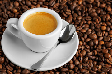 White espresso cup filled with fresh aromatic coffee, resting on bed of roasted beans, accompanied...