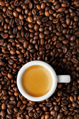 Top view of white espresso cup stands on roasted beans, highlighting rich crema and creating background for coffee lovers. Vertical shoot