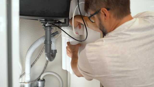 Man installs water purifier. Replacement water filter with cartridges in kitchen under kitchen sink.