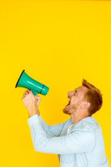 Side view portrait of a young man shouting with a megaphone on a yellow background, expressing his protest or sharing important news