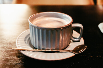 A ceramic coffee cup on a saucer and a long copper spoon. Serving a drink in a cafe.