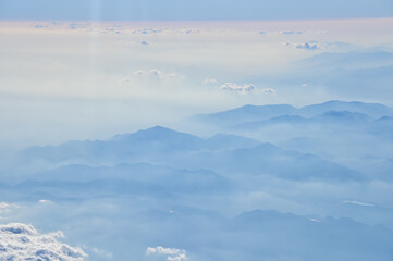 The view of the stunning landscape with mountains and clouds from the airplane window. Aerial view of the natural scene, mountain range. Travel and landscape scene. Travel and nature concept. 