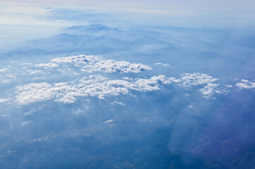 The view of the stunning landscape with mountains and clouds from the airplane window. Aerial view of the natural scene, mountain range. Travel and landscape scene. Travel and nature concept. 