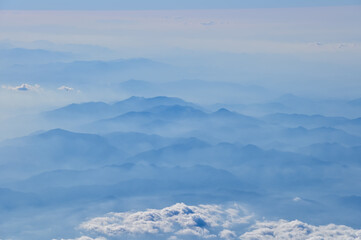 The view of the stunning landscape with mountains and clouds from the airplane window. Aerial view of the natural scene, mountain range. Travel and landscape scene. Travel and nature concept. 