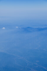 The view of the stunning landscape with mountains and clouds from the airplane window. Aerial view of the natural scene, mountain range. Travel and landscape scene. Travel and nature concept. 